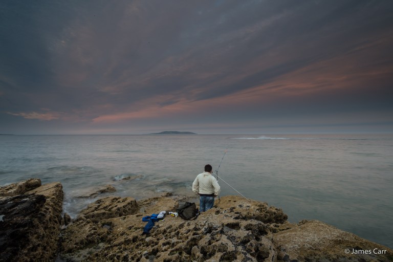 A fisherman watches a jet ski go by